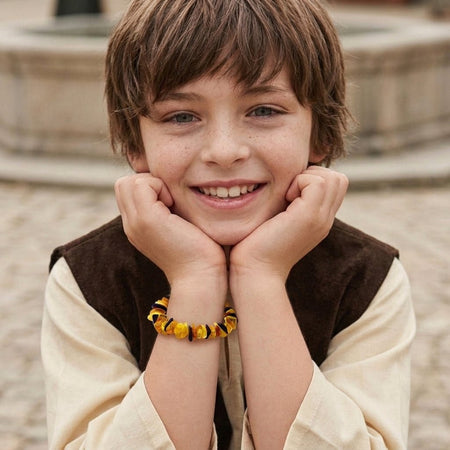 Bambino sorridente che indossa un bracciale in ambra russa naturale al polso.