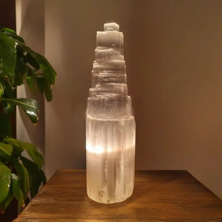 Lampada in selenite naturale a forma di torre accesa con luce calda